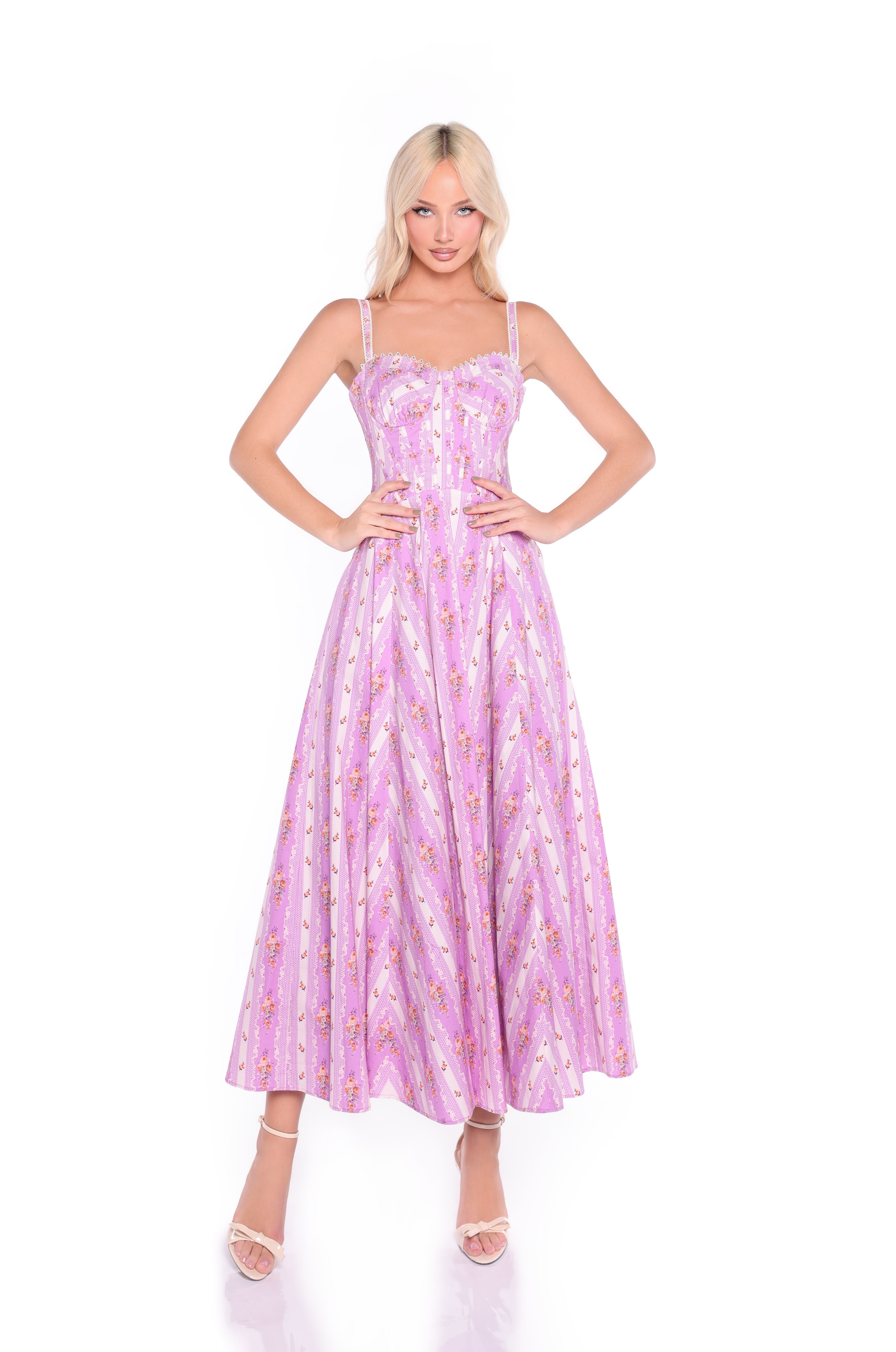 A woman stands against a white background wearing the Rosella Lavender Lilac Floral Casual Midi Dress, which features a floral print, sleeveless design, fitted corset bodice, and flared skirt.
